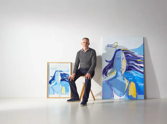 Artista sentado junto a sus cuadros